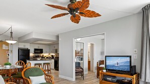 A modern living room with a television, wicker furniture, and a ceiling fan.