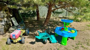 Outdoor toys and equipment, including a toy tractor, a toy shovel, and a toy watering can, in a grassy area with trees. - Ferienhaus Havelzeit in Werder an der Havel (Werder an der Havel)