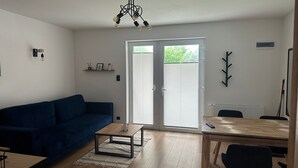 A living room with a blue sofa, a wooden coffee table, and a dining table with chairs. There is a ceiling light fixture and a radiator on the wall. - Holiday apartments very close to the beach (Chlopy)