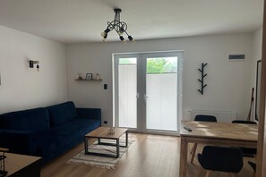 A living room with a blue sofa, a coffee table, a dining table with chairs, and a ceiling light fixture.