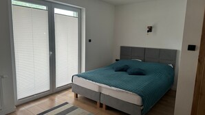 A bedroom with a bed, a grey headboard, a window with blinds, and a small wall-mounted light. - Holiday apartments very close to the beach (Chlopy)