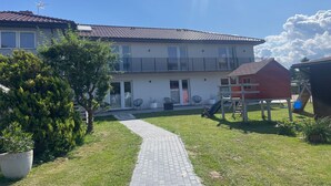 A two-story building with a tiled roof, a paved pathway leading to the entrance, and a small red structure nearby. - Holiday apartments very close to the beach (Chlopy)