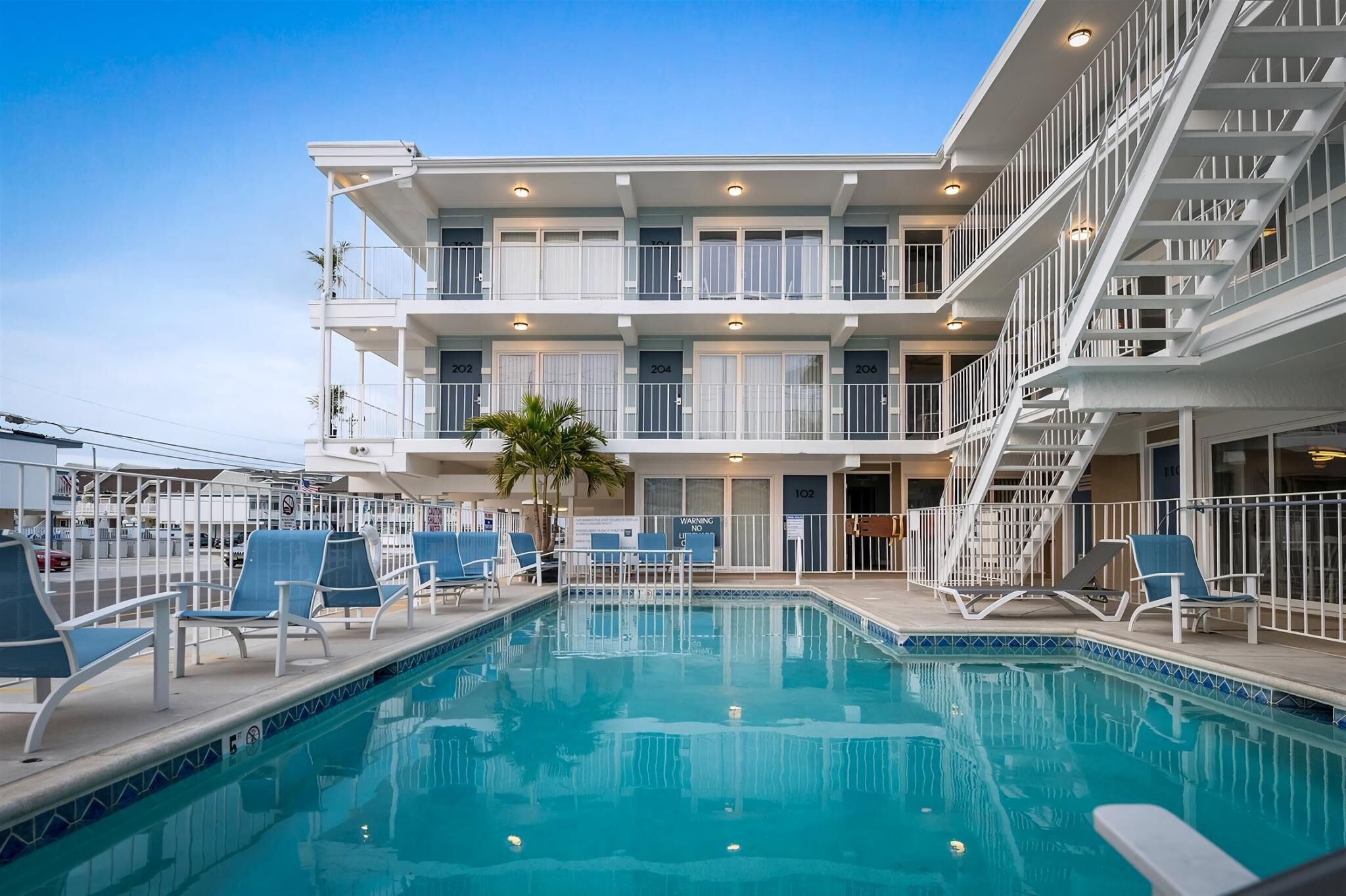 A multi-story hotel with a swimming pool, balconies, and a staircase.
