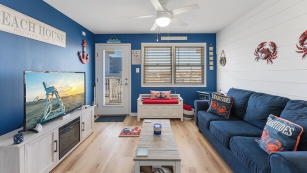 A living room with a TV, a ceiling fan, a blue couch, and a white bench.