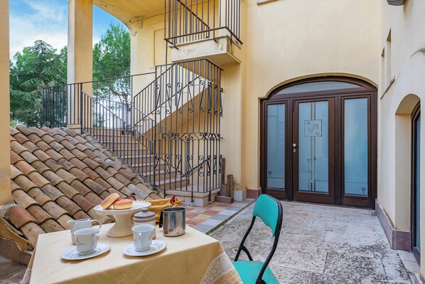 A terrace with a table set for tea, a chair, a staircase, and a door with a sign. - Nella Apartment With Pool (Sannicandro di Bari)