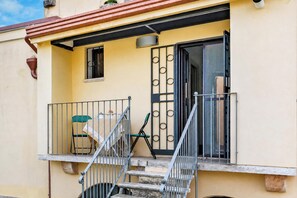 A balcony with a chair, a small table, and a window with a metal gate. - Nella Apartment With Pool (Sannicandro di Bari)