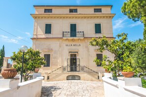 A building with the sign 'VILLA NELLA' at the entrance, a stone-paved courtyard, and potted plants around. - Nella Apartment With Pool (Sannicandro di Bari)