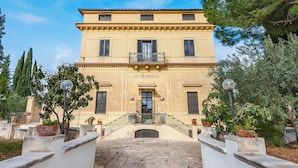 A two-story building with a central entrance, potted plants, and a stone pathway leading to the entrance. - Nella Apartment With Pool (Sannicandro di Bari)