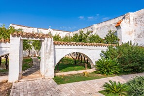 A white building with a tiled roof, a stone pathway, and green plants. - Nella Apartment With Pool (Sannicandro di Bari)