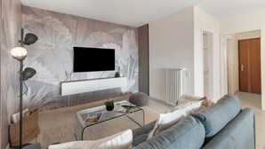 A modern living room with a flat-screen TV mounted on the wall, a sofa, a coffee table, and a floor lamp. - Residenza Tasso Sul Lago in Castagnola (Lugano)