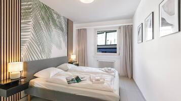 Ein modernes Hotelzimmer mit einem großen Bett, Nachttischlampen, einem Fenster mit Vorhängen und gerahmten Bildern an der Wand.