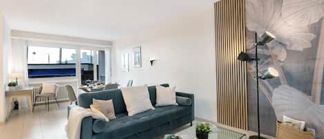 Ein modernes Wohnzimmer mit einem blauen Sofa, einem Glastisch, einer Stehlampe und einer großen Wandmalerei mit floralem Muster.