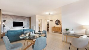 A modern living room with a blue sofa, a dining table with chairs, a TV mounted on the wall, and a kitchen area with cabinets and a countertop. - Residenza Tasso Sul Lago in Castagnola (Lugano)