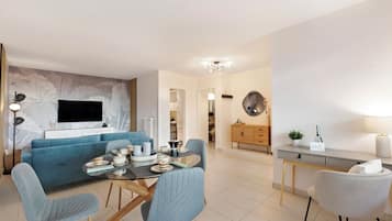 Ein modernes Wohnzimmer mit einem blauen Sofa, einem Esstisch mit Stühlen, einem an der Wand befestigten Fernseher und einer Küchenzeile mit Schränken und einer Arbeitsplatte.