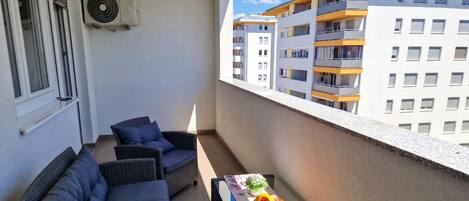 A balcony with wicker furniture, a table with fruit, and a view of adjacent buildings.
