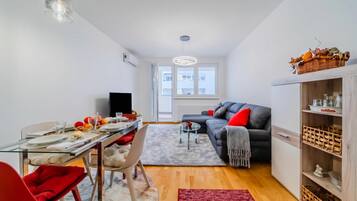 A modern living room with a dining area, a grey sofa, a red chair, a glass coffee table, and a red rug.