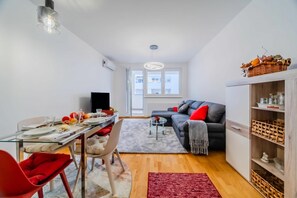 A modern living room with a dining area, a grey sofa, a red chair, a glass coffee table, and a red rug. - Modern Oasis With Terrace (Zagreb)