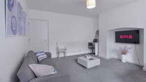 Un salon moderne avec un canapé gris, une table basse blanche et un téléviseur à écran plat affichant le logo « NETFLIX ».