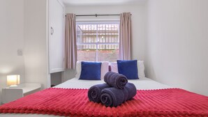 Une chambre d’hôtel avec un lit, deux oreillers, une couverture rouge et une fenêtre avec des rideaux.