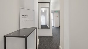 Un couloir orné d’un tableau encadré où figure une définition du mot « voyage », un miroir qui reflète le couloir, et un sol recouvert de moquette.
