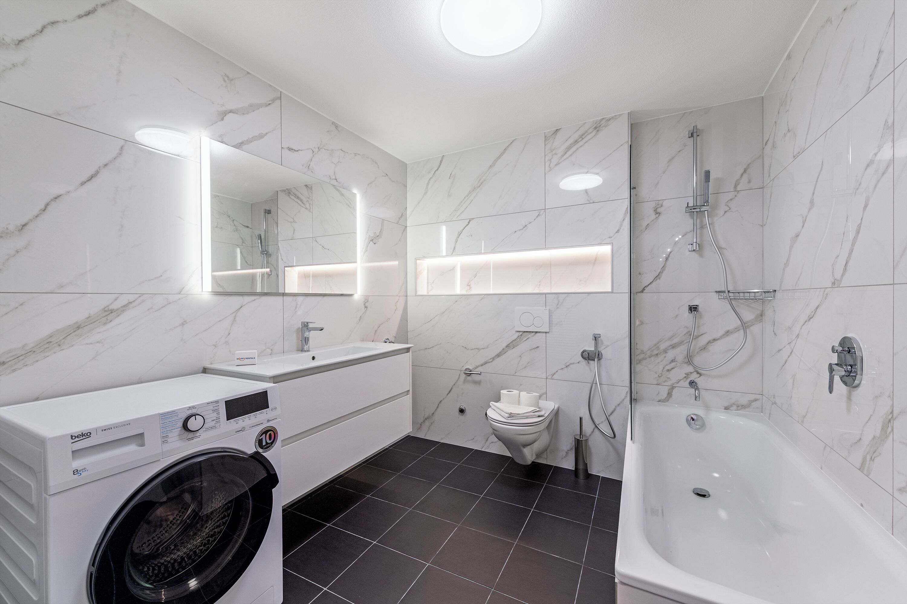 Een moderne badkamer met een wasmachine, toilet en bad.