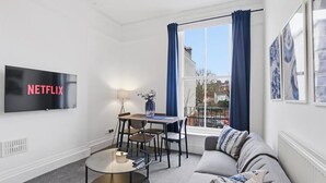 A modern living room with a flat-screen TV, a round coffee table, a sofa, and a dining table with chairs. - Well-appointed Stylish Apartment in Central Gloucester (Gloucestershire)