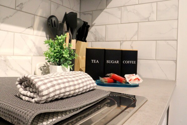 Una encimera de cocina con un toallón de cuadros, una pequeña planta en maceta, un bloque de cuchillos y una bandeja con té, azúcar y cajas de café.