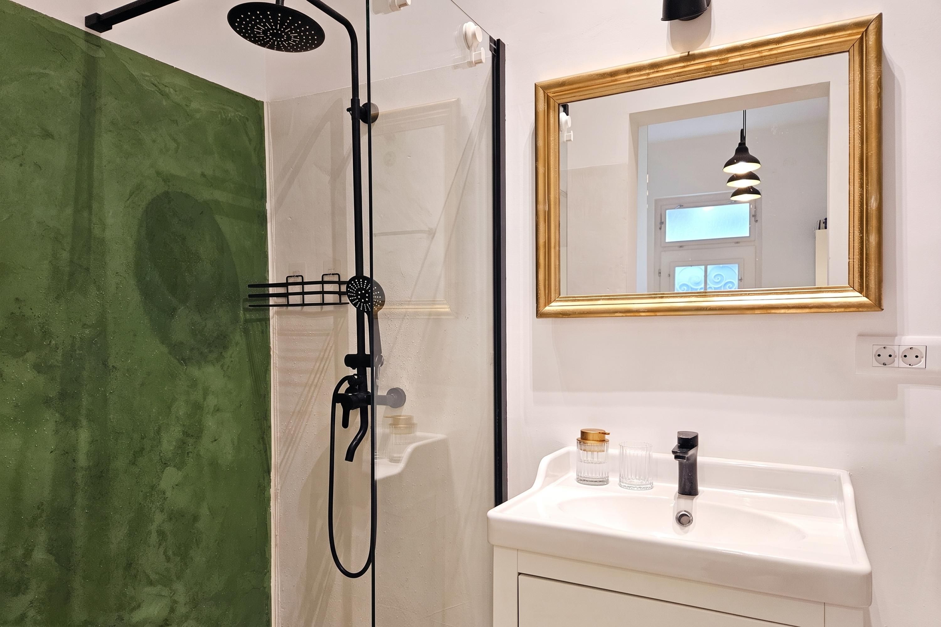 A bathroom with a shower, a sink with a mirror, and a green wall.