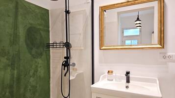 A bathroom with a shower, a sink with a mirror, and a green wall.