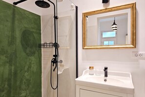 Une salle de bain avec une douche, un lavabo avec un miroir et un mur vert.