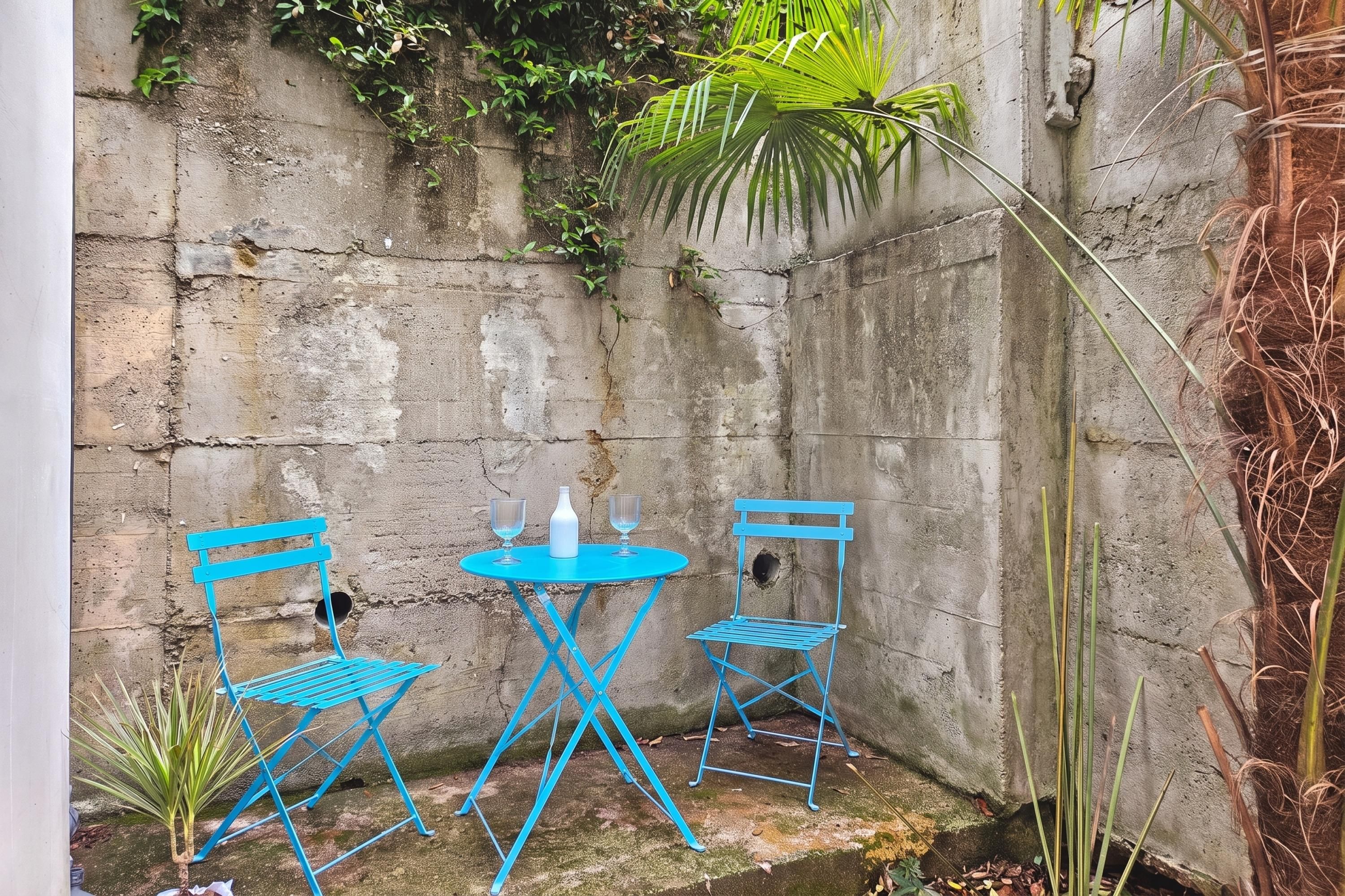 A small outdoor seating area with a blue metal table and chairs, a white bottle, and a small plant.