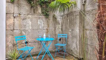 A small outdoor seating area with a blue metal table and chairs, a white bottle, and a small plant.