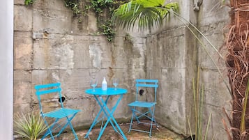 A small outdoor seating area with a blue metal table and chairs, a white bottle, and a small plant.