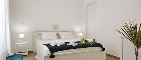 A hotel room with a bed, bedside tables, a bedside lamp, a green cushion, a plant, and a wall-mounted light fixture.