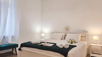 A hotel room with a bed, a bedside table with a lamp, a bench, and a window with curtains.