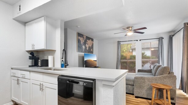 A compact kitchen with white cabinets, a dishwasher, and a coffee machine. There's a ceiling fan and a window with blinds. - Beautiful 1BD/1BA in University Hills jkxg (Austin)