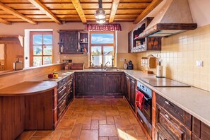 A kitchen with wooden cabinets, a large island, and a view of the outdoors through a window. - Balaton View From Almadi With Terrace & Garden (Balatonalmadi)