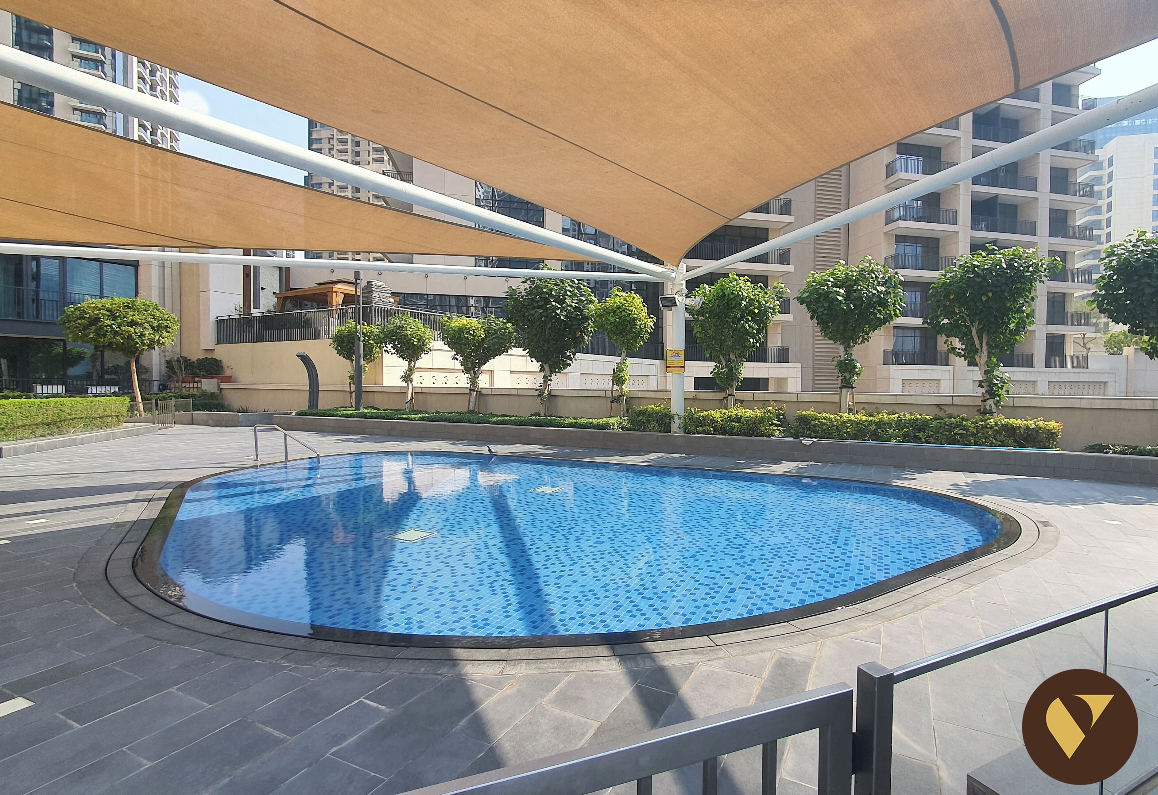 Una piscina moderna al aire libre con borde de azulejos, rodeada por una zona pavimentada y una estructura tipo marquesina.