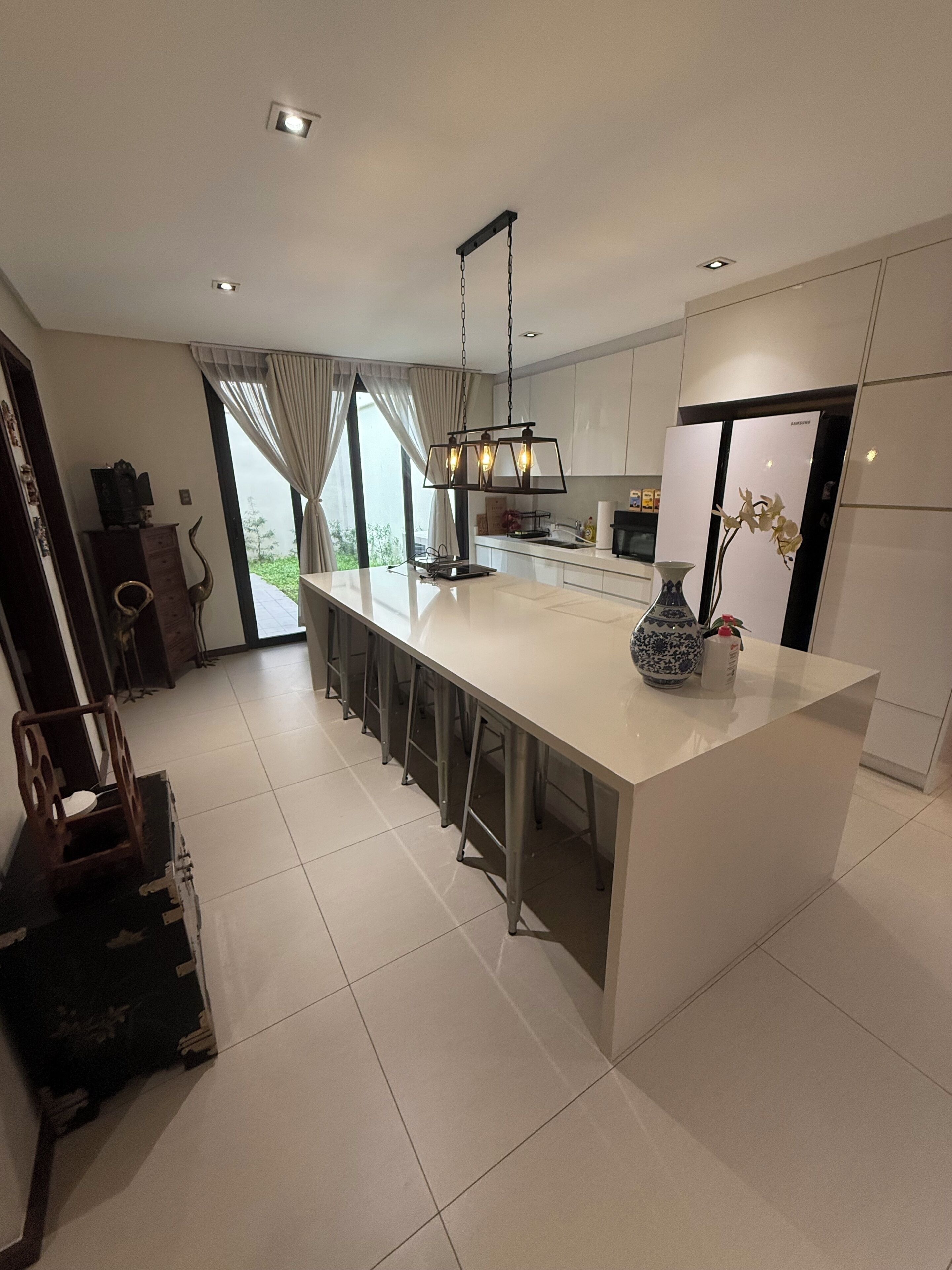 A modern kitchen with a central island, pendant lighting, and a refrigerator.