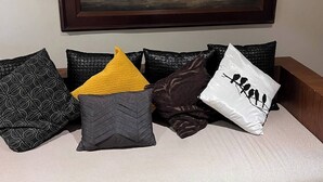 En sofa med diverse puder med mønstre og et indrammet billede af en bygning.