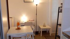 A small, clean room with a white table, chairs, a lamp, and a refrigerator. - Downstairs nature studio (Grenoble)