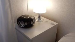 A small bedside table with a white lamp and a black electronic device, possibly a speaker, on it. - Downstairs nature studio (Grenoble)