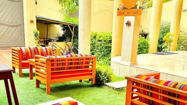 Un área de estar al aire libre con bancos de madera y cojines coloridos, rodeada de follaje y un letrero que dice "Smile Space".