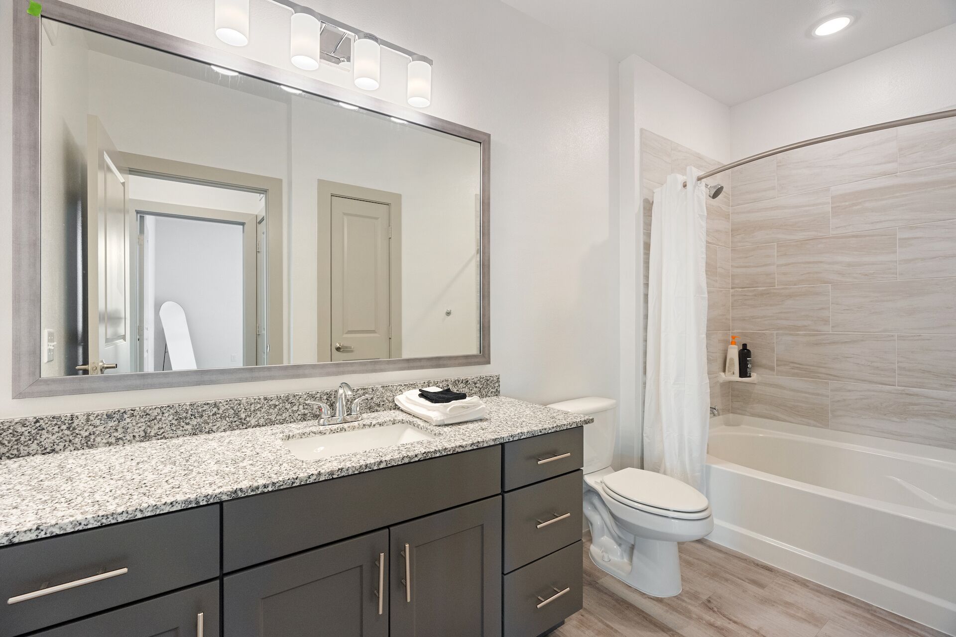 Une salle de bain moderne avec un comptoir en granit, un grand miroir, des toilettes et une douche à l’italienne.