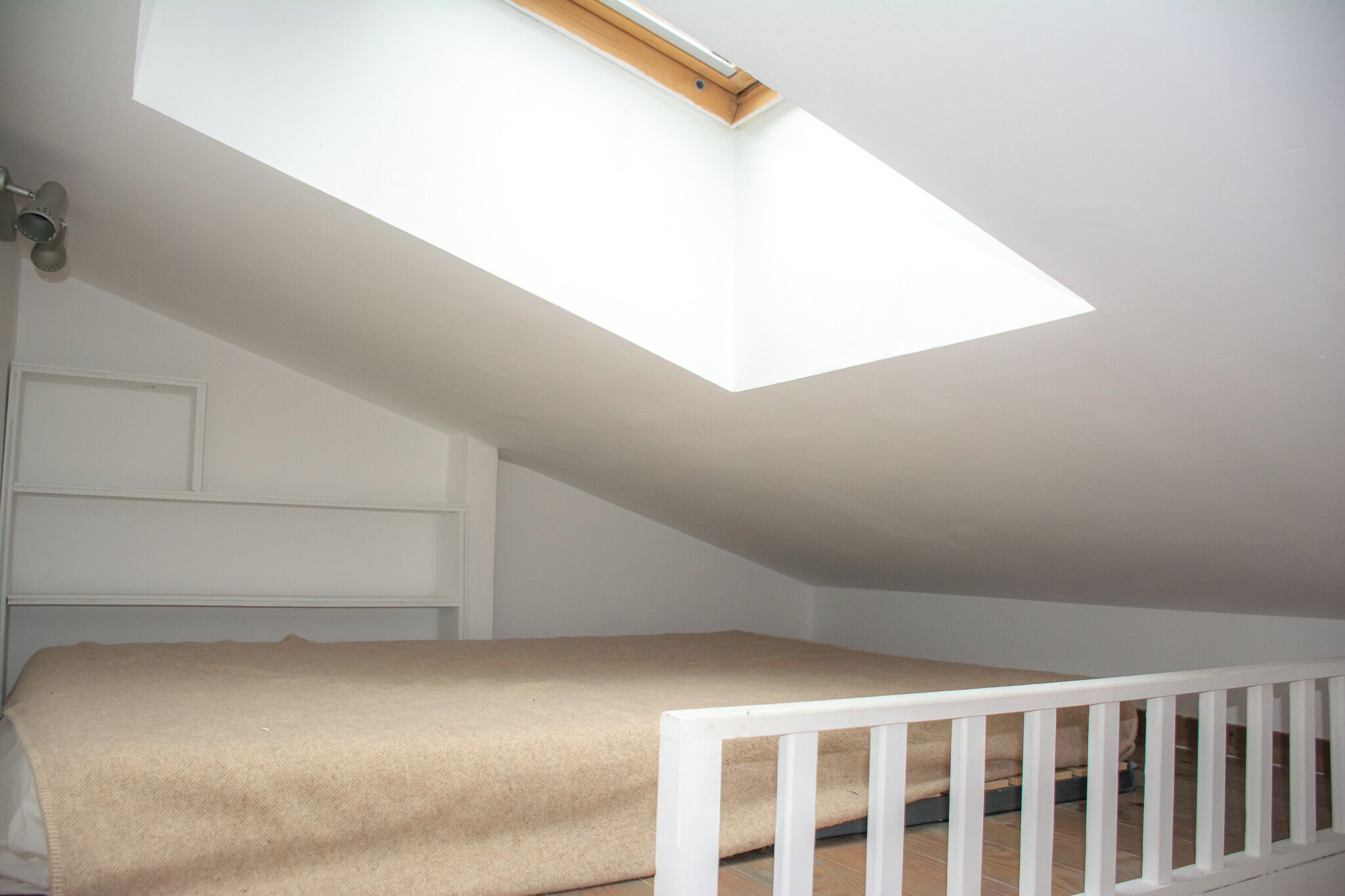A room with a sloped ceiling, a skylight, a white crib, and a white door.