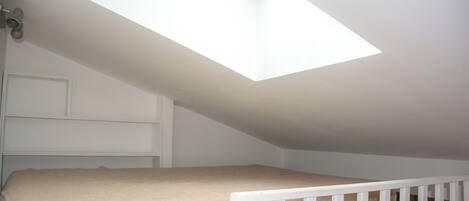 A room with a sloped ceiling, a skylight, a white crib, and a white door.