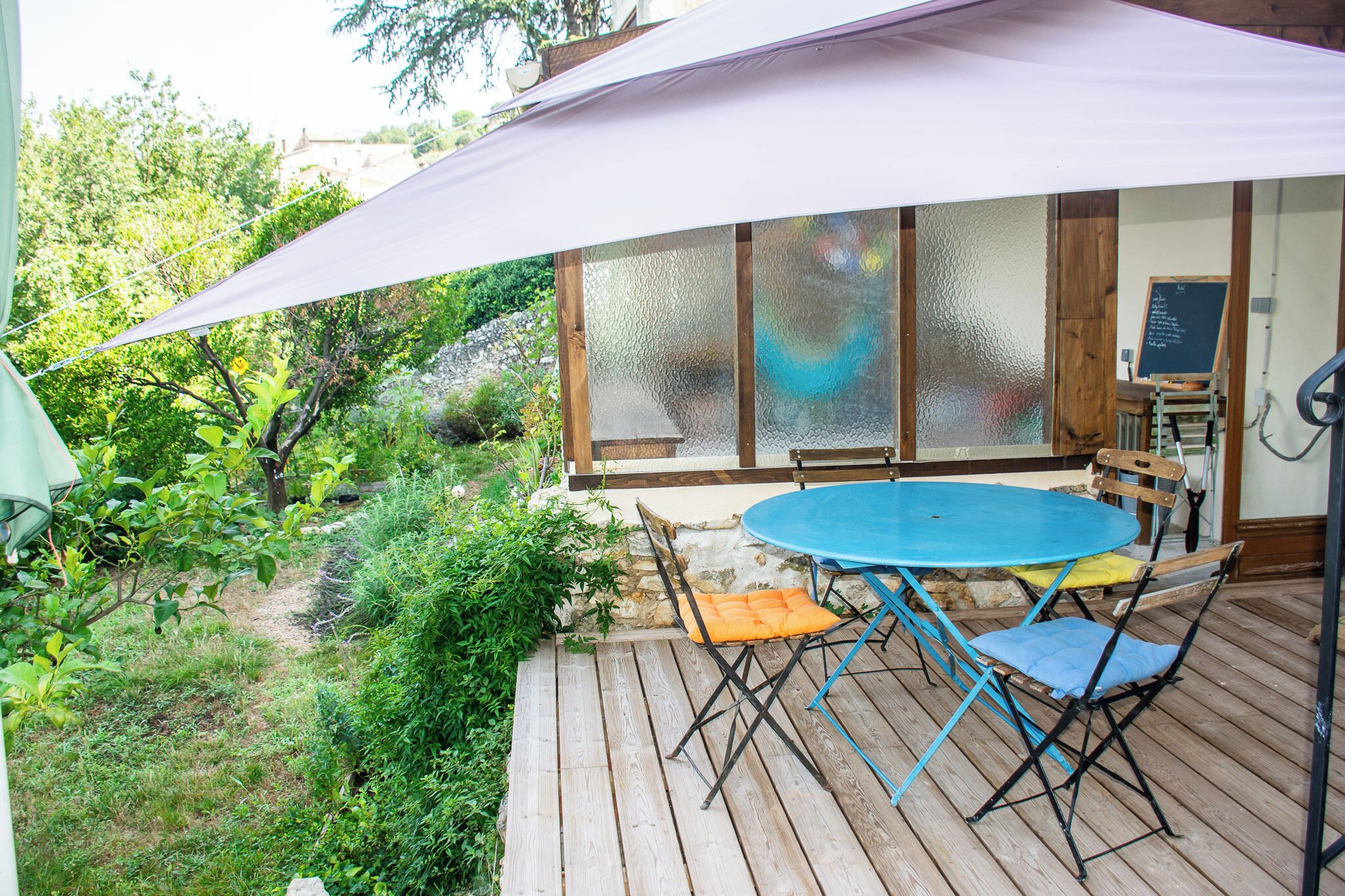 Eine Holzdiele mit blauem Tisch und Stühlen, einem weißen Sonnenschirm und einer Tafel mit Schrift.