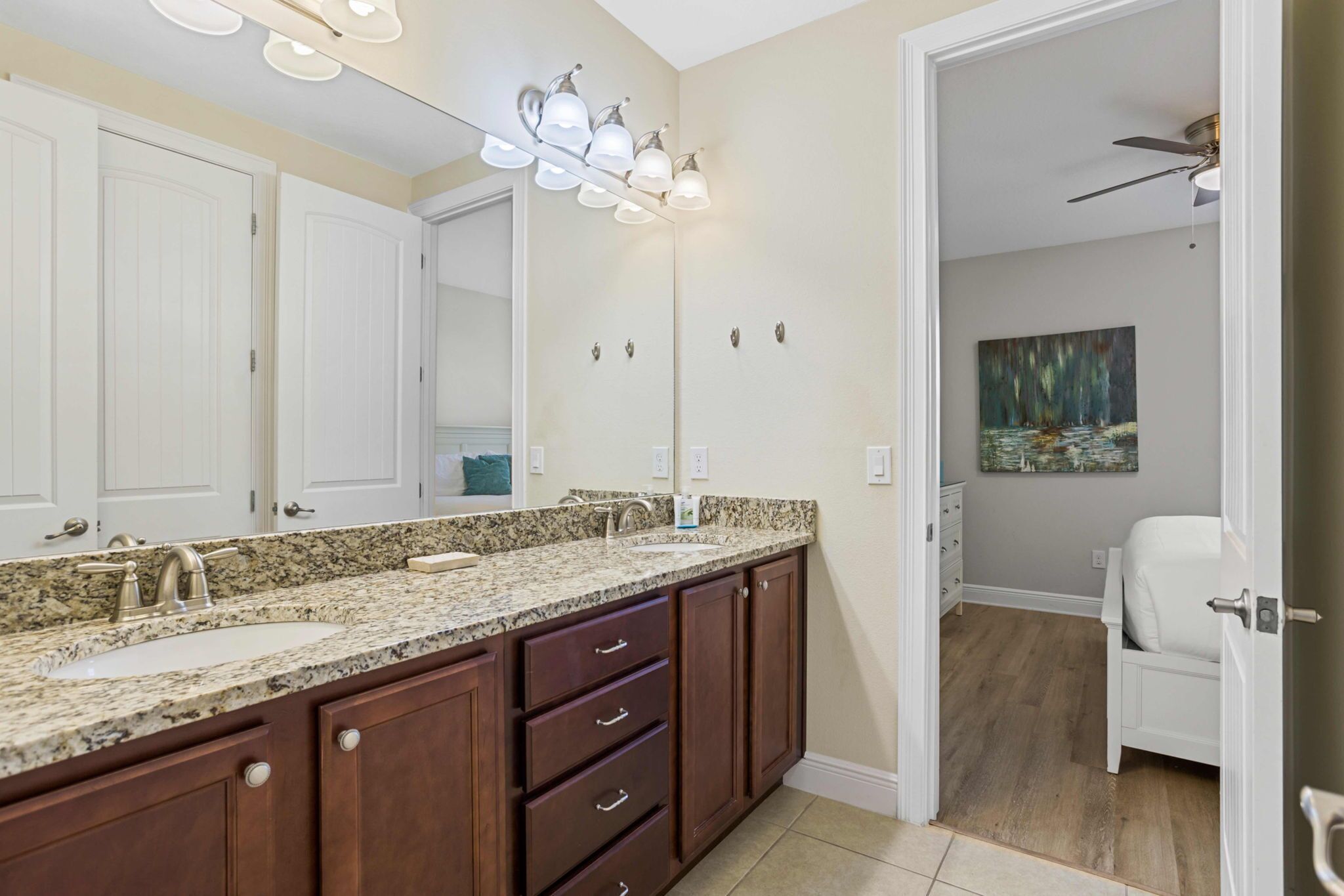 A bathroom with a granite countertop, two sinks, a large mirror, and a ceiling fan.
