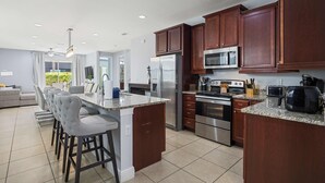A modern kitchen with dark wooden cabinets, stainless steel appliances, and a granite countertop. - Modern Villa / Movie Room, Private Pool & Spa/10 Mins to Disney + Free WiFi (Kissimmee)