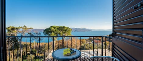 Un balcón con mesa y sillas, con vista a un cuerpo de agua y montañas distantes.